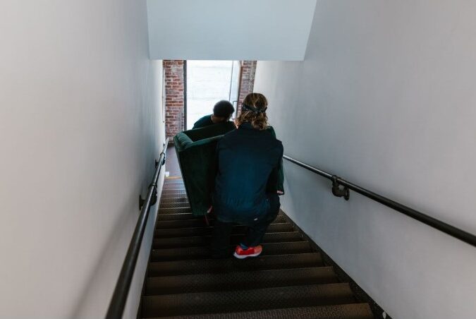 Furniture movers carrying a couch down a narrow Woodstock staircase in Cape Town